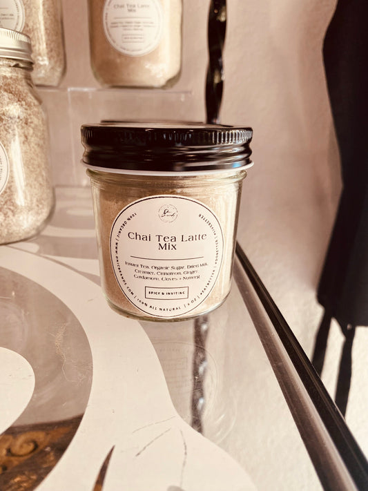 Creamy chai tea latte in a glass cup with frothy top, served with a cinnamon stick and sprinkled with spices.