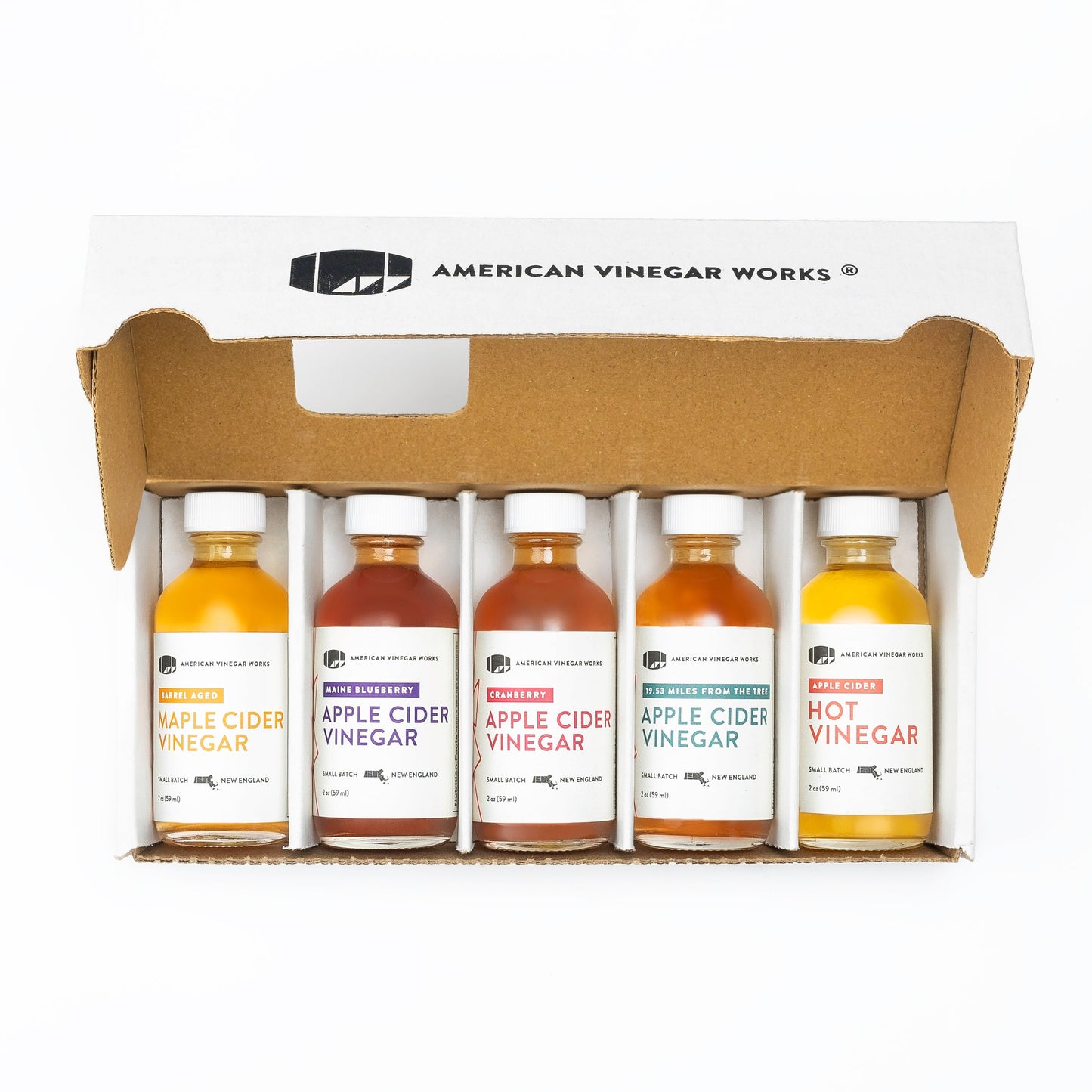 Open box of American Vinegar Works apple cider vinegar sampler pack with five barrel-aged vinegar bottles arranged for tasting.