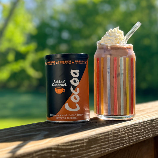 Cup of Fireside Coffee Co. salted caramel cocoa in a mug, topped with whipped cream and caramel drizzle, served on a cozy wooden table.