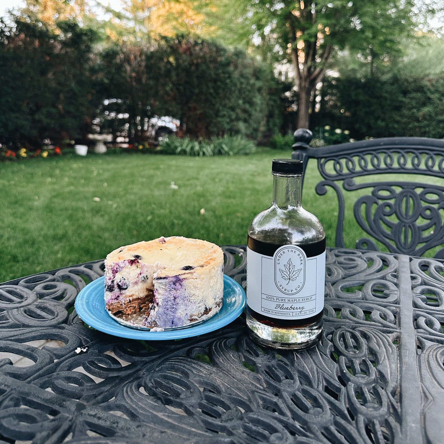 Glass bottle of blueberry maple syrup from Under The Bark Syrup Co with fresh blueberries and maple leaves.