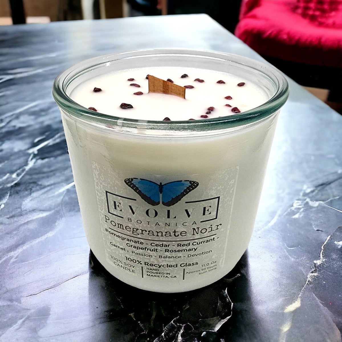 Evolve Botanica Rocks Candle with Pomegranate Noir scent, featuring a wood wick and garnet gemstone in a soy candle setting.