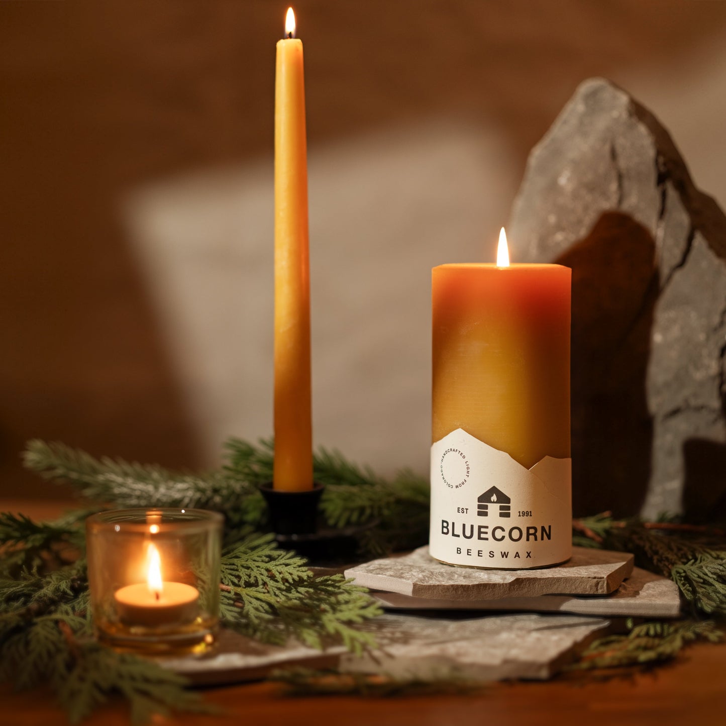 Pair of Bluecorn Candles hand-dipped beeswax taper candles with pine and stone accents, shown alongside tea lights.