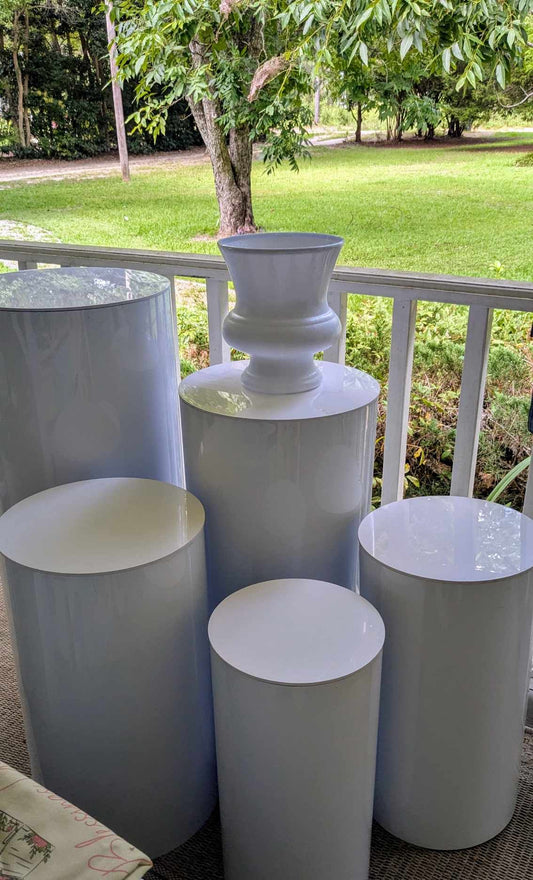 White pedestal stand and cylinder tables for event rentals by Blessings Grow Meadows Merch, ideal for elegant gatherings.