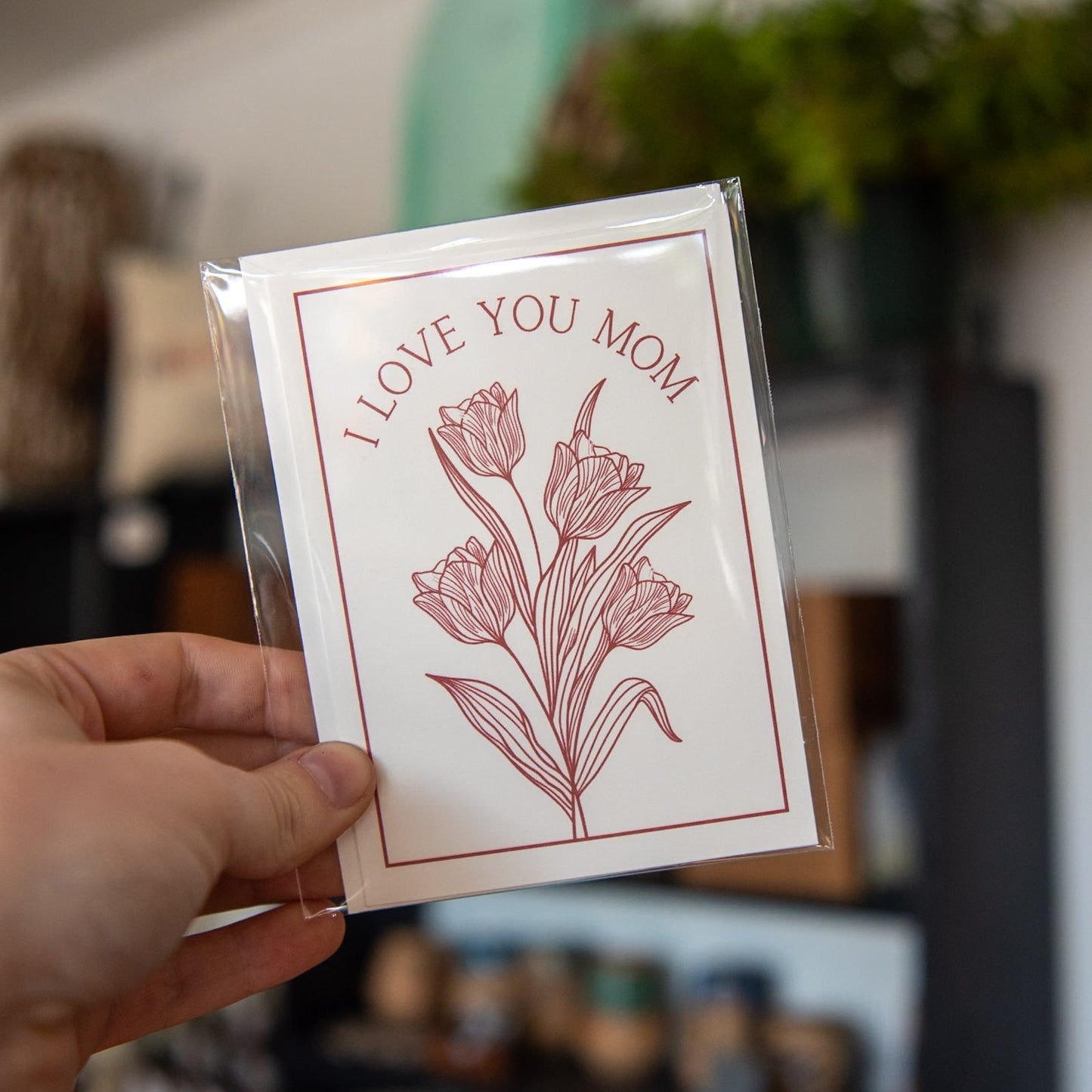 Still Magnolia "I Love You Mom" card with floral design, featuring heartfelt message, perfect for Mother's Day or special occasions.