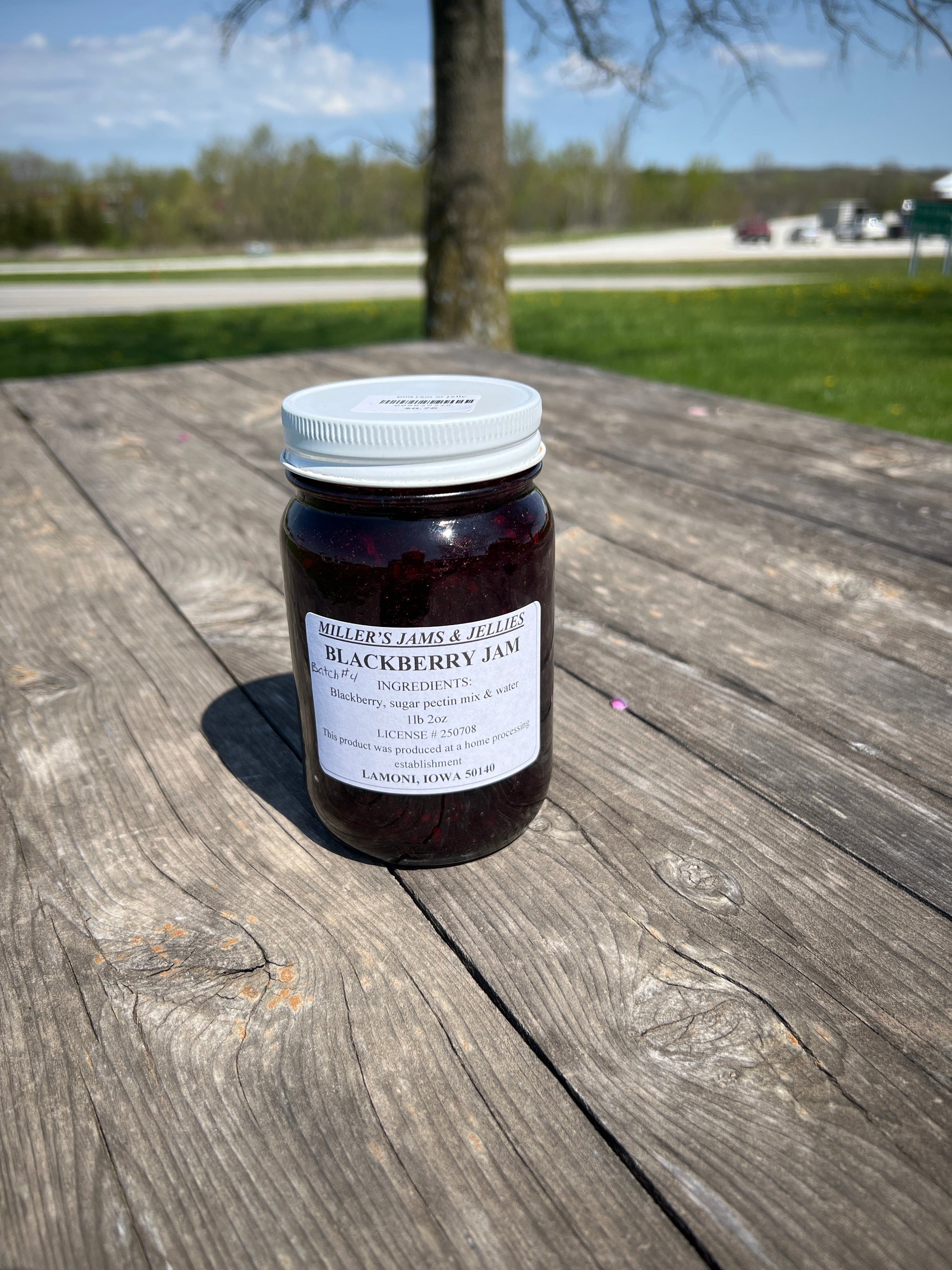 Jar of Amish Miller’s Blackberry Jam with fresh blackberries and rural farmhouse background, showcasing Amish Country Store product.