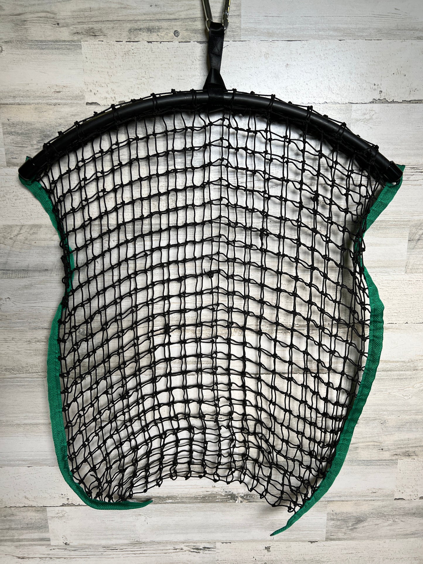 Green regular haynet from Haylo Haynets, LLC filled with hay, hanging in a barn setting for horse feeding.