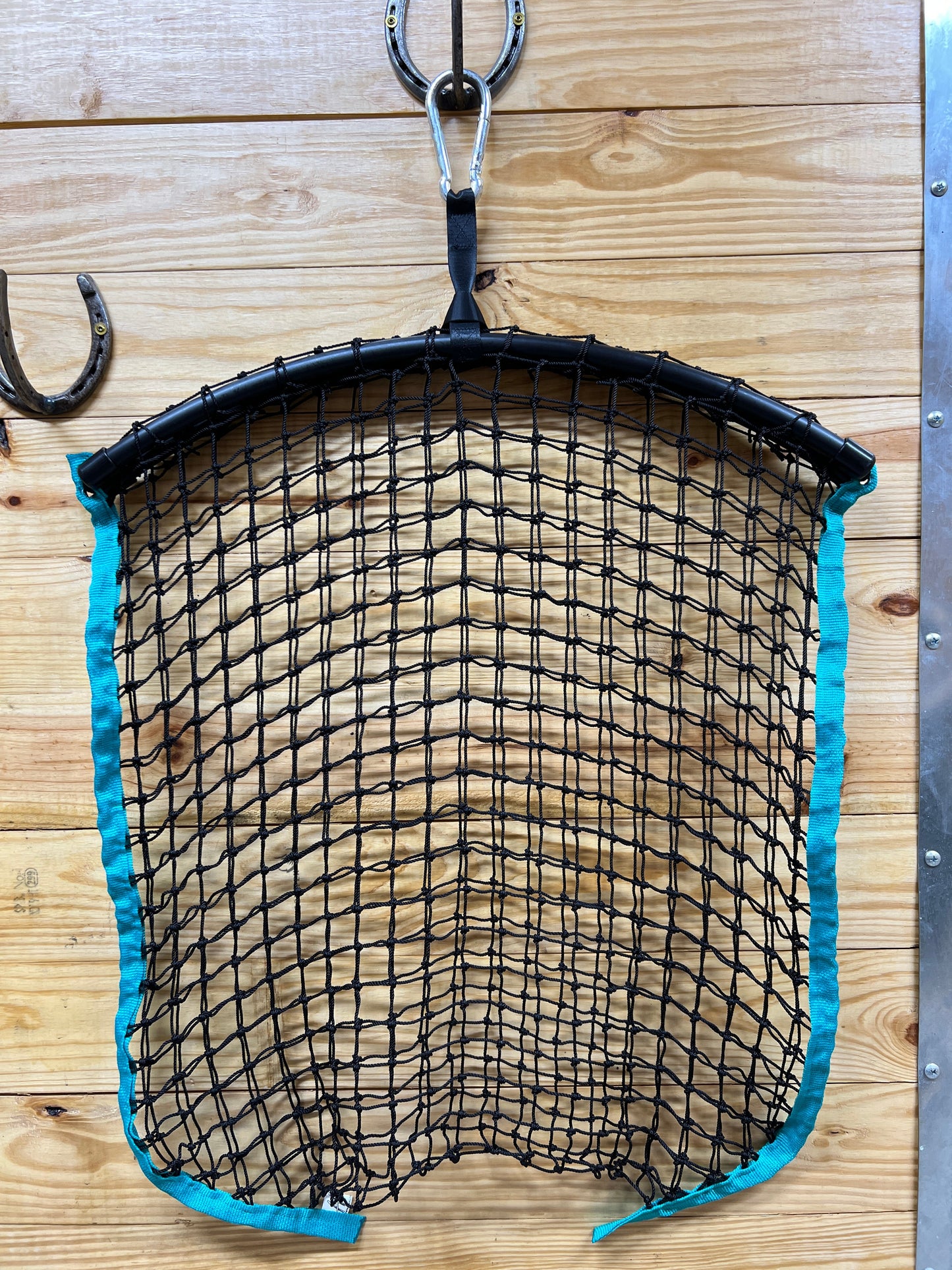 Teal regular haynet from Haylo Haynets, LLC with durable netting and metal hooks for easy hay storage and feeding.