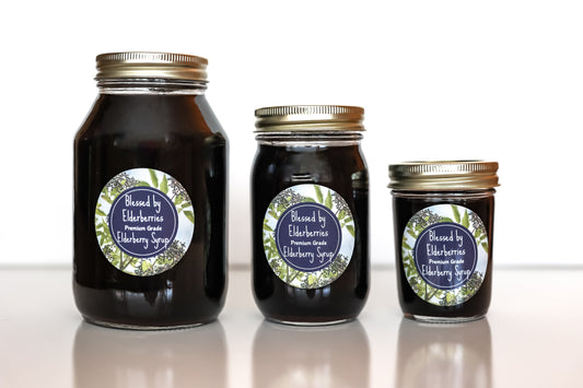Bottle of Blessed by Elderberries elderberry syrup with fresh elderberries and honey on a wooden surface.
