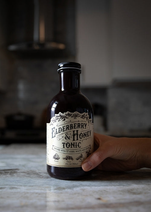 Elderberry and honey tonic bottle from Roots and Leaves LLC, close-up showing label and amber liquid inside.
