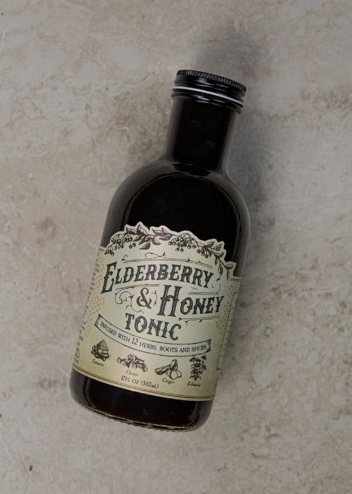 Elderberry and honey tonic in a glass bottle with fresh elderberries and honey drizzles, produced by Roots and Leaves LLC.