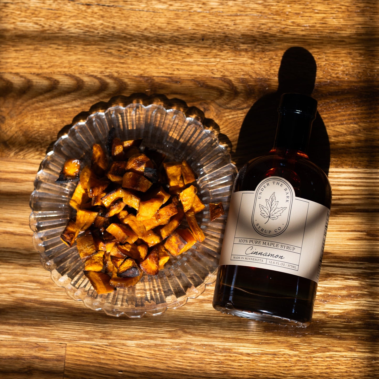 Bottle of Cinnamon Maple Syrup from Under The Bark Syrup Co showing the label and syrup inside the clear glass bottle.