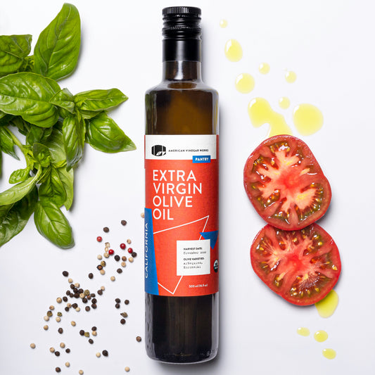 Bottle of American Vinegar Works organic extra virgin olive oil with a green label and gold cap on a wooden surface.