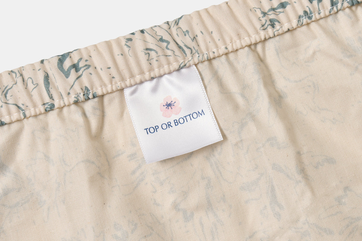Blue botanical print cotton bed sheet set by American Blossom Linens on natural background, showing elastic edges and top/bottom labels.