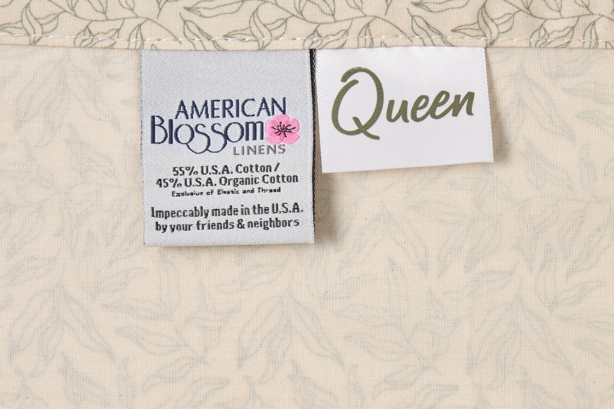 Green leaf print cotton bed sheet set from American Blossom Linens on natural background, showing size label and fabric details.