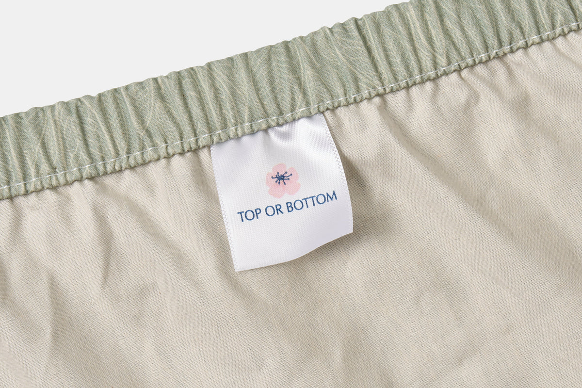 Cotton bed sheet set with leaf print on green background by American Blossom Linens, featuring elastic fitted corners and a top label.