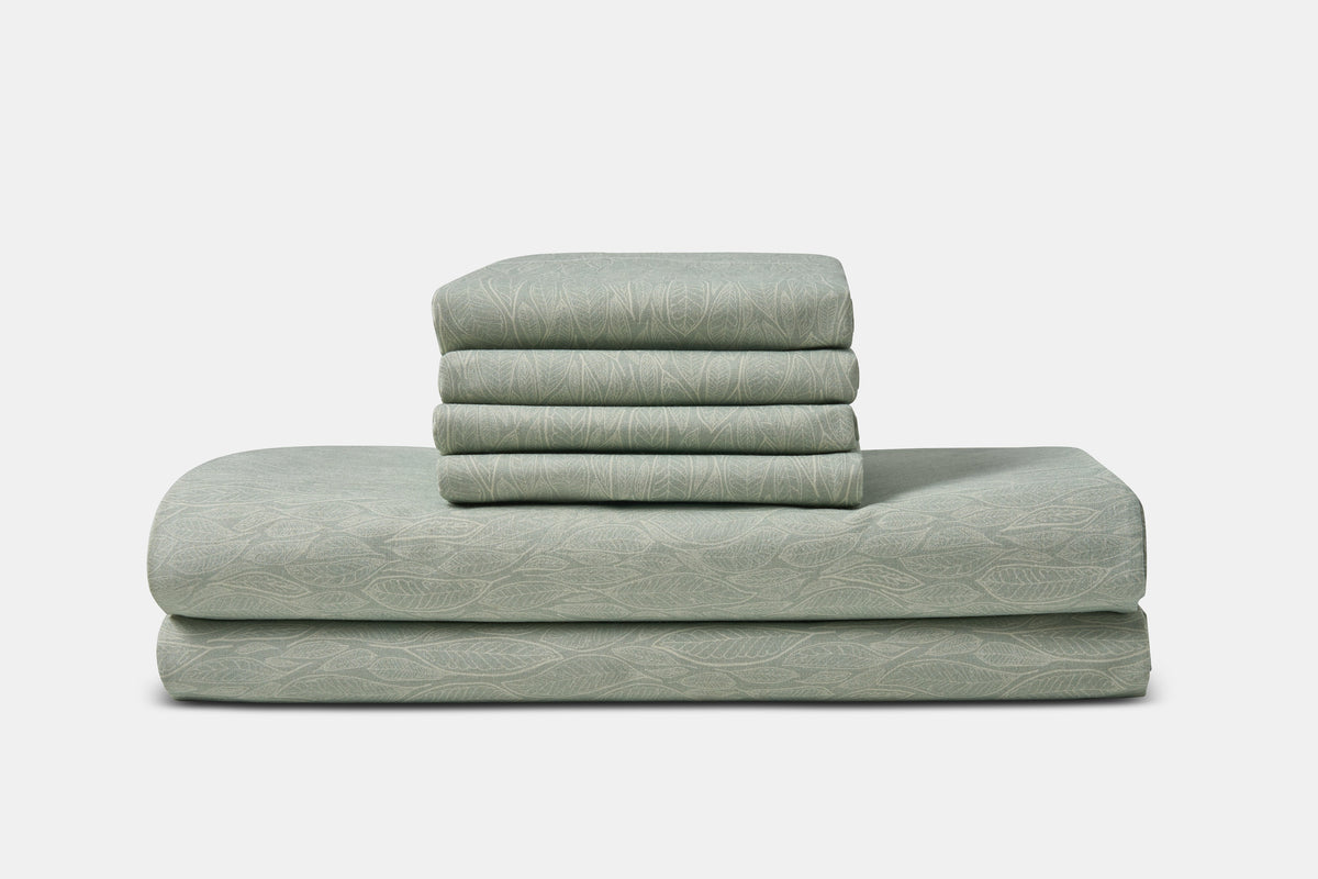 American Blossom Linens cotton bed sheet set with green leaf print on a cozy bed setup.