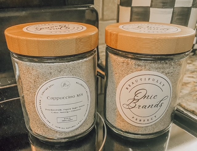Onic Brands LLC cappuccino drink mix in a jar, with a scoop and prepared cappuccino in a cup showing frothy top.