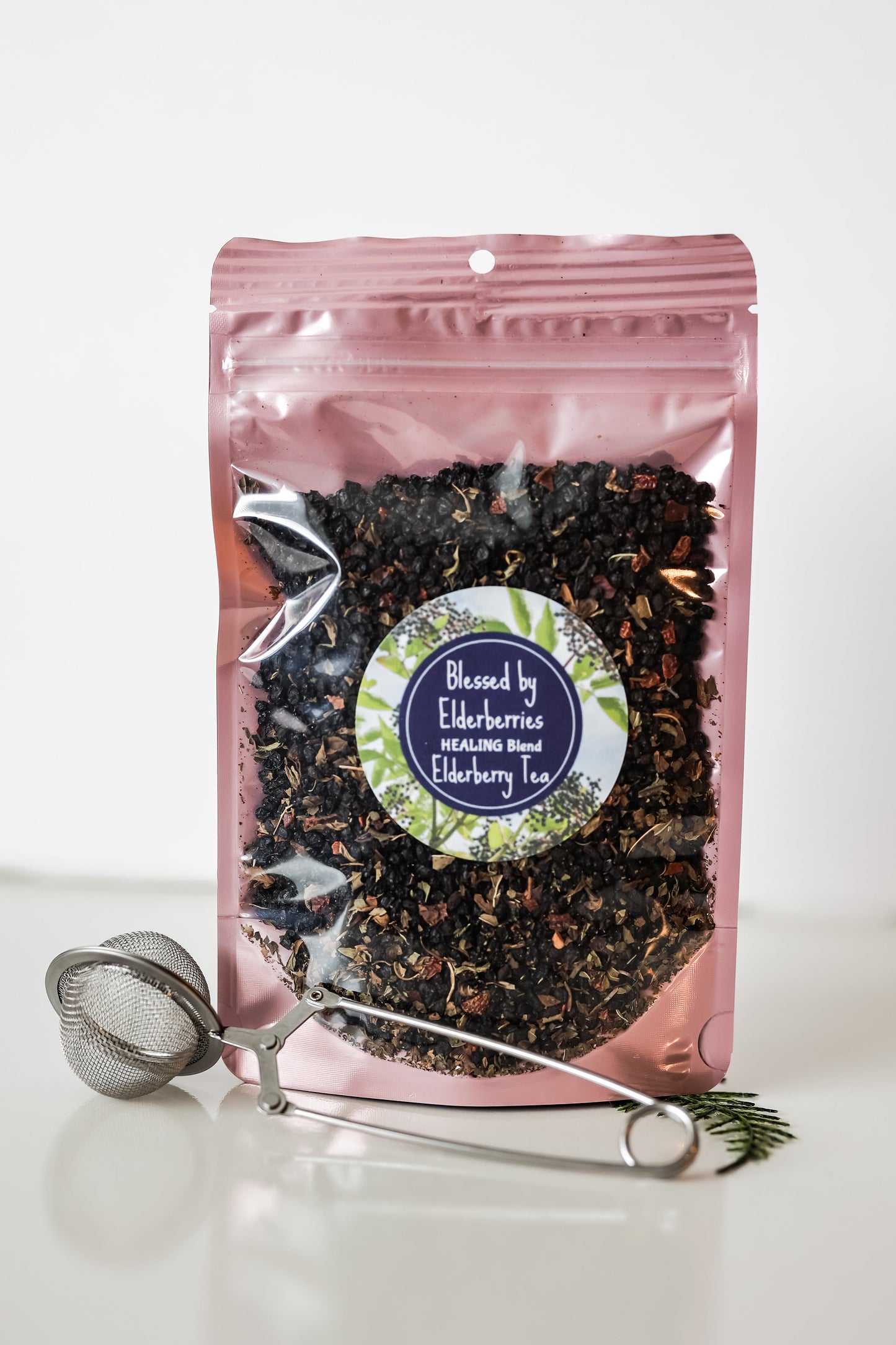 Healing blend Elderberry tea by Blessed by Elderberries in a tea infuser with dried elderberries and herbs on a wooden surface.