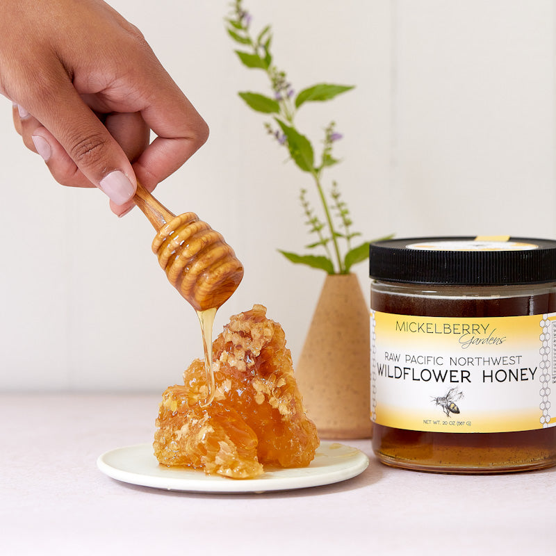Jar of raw single-source honey from Mickelberry Gardens, shown in a kitchen setting. Natural, golden honey with a wooden honey dipper.