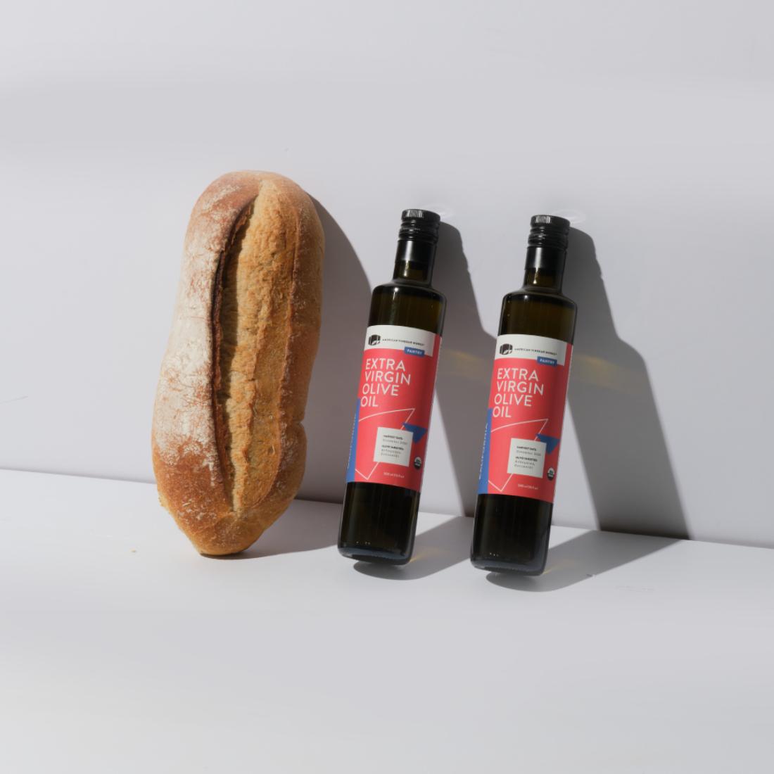 Organic California extra virgin olive oil in a glass bottle, highlighting American Vinegar Works branding and fresh olive oil appearance.