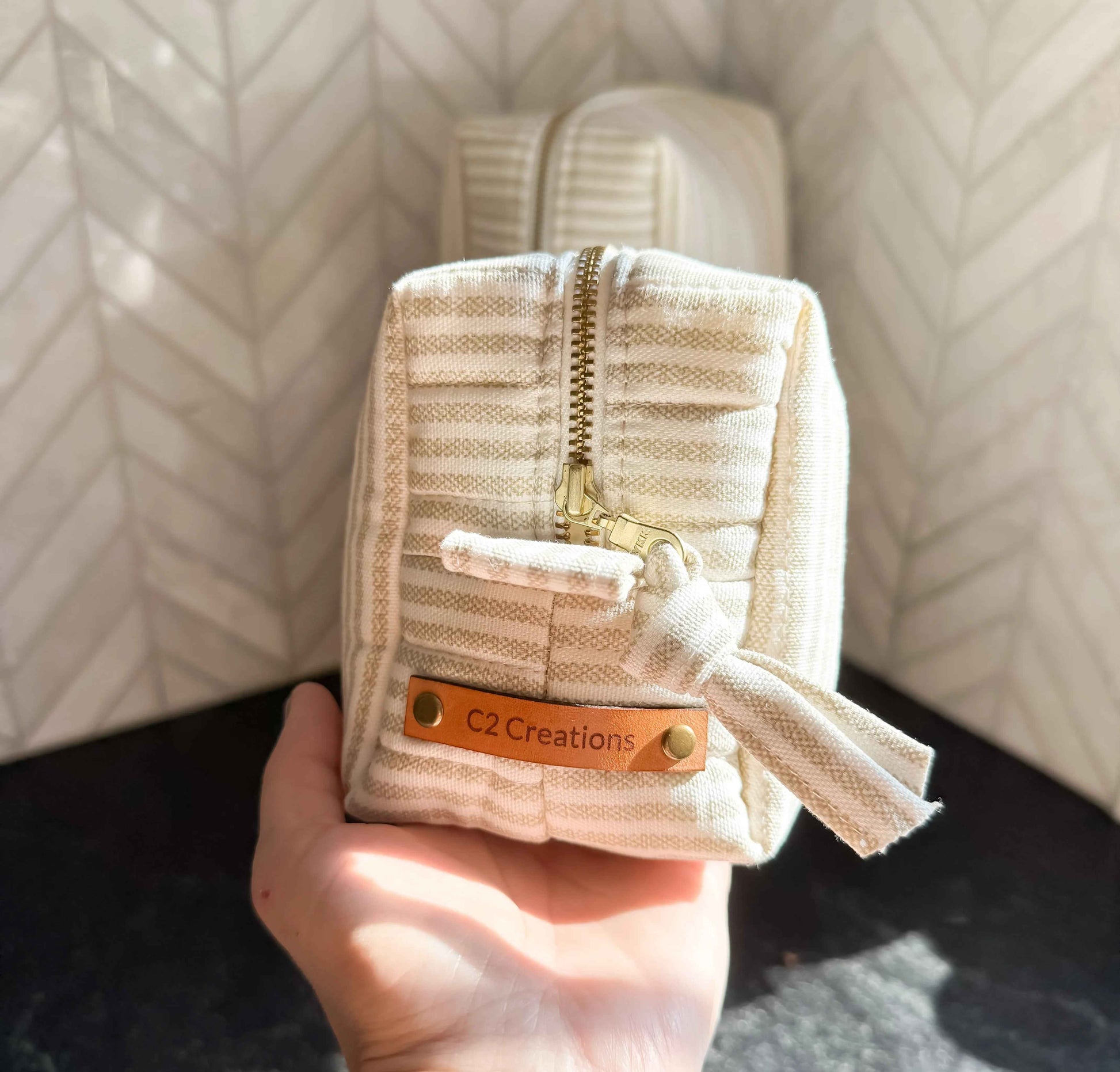 Handmade C2 Creations LLC boxy makeup and toiletry bag in taupe and cream ticking stripe pattern, with zipper closure and compact design.