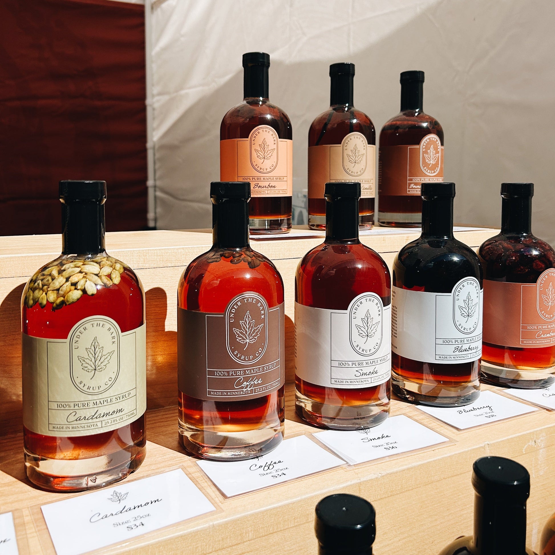 Bottle of Smoke Maple Syrup from Under The Bark Syrup Co with a dark amber color, placed on a wooden surface.