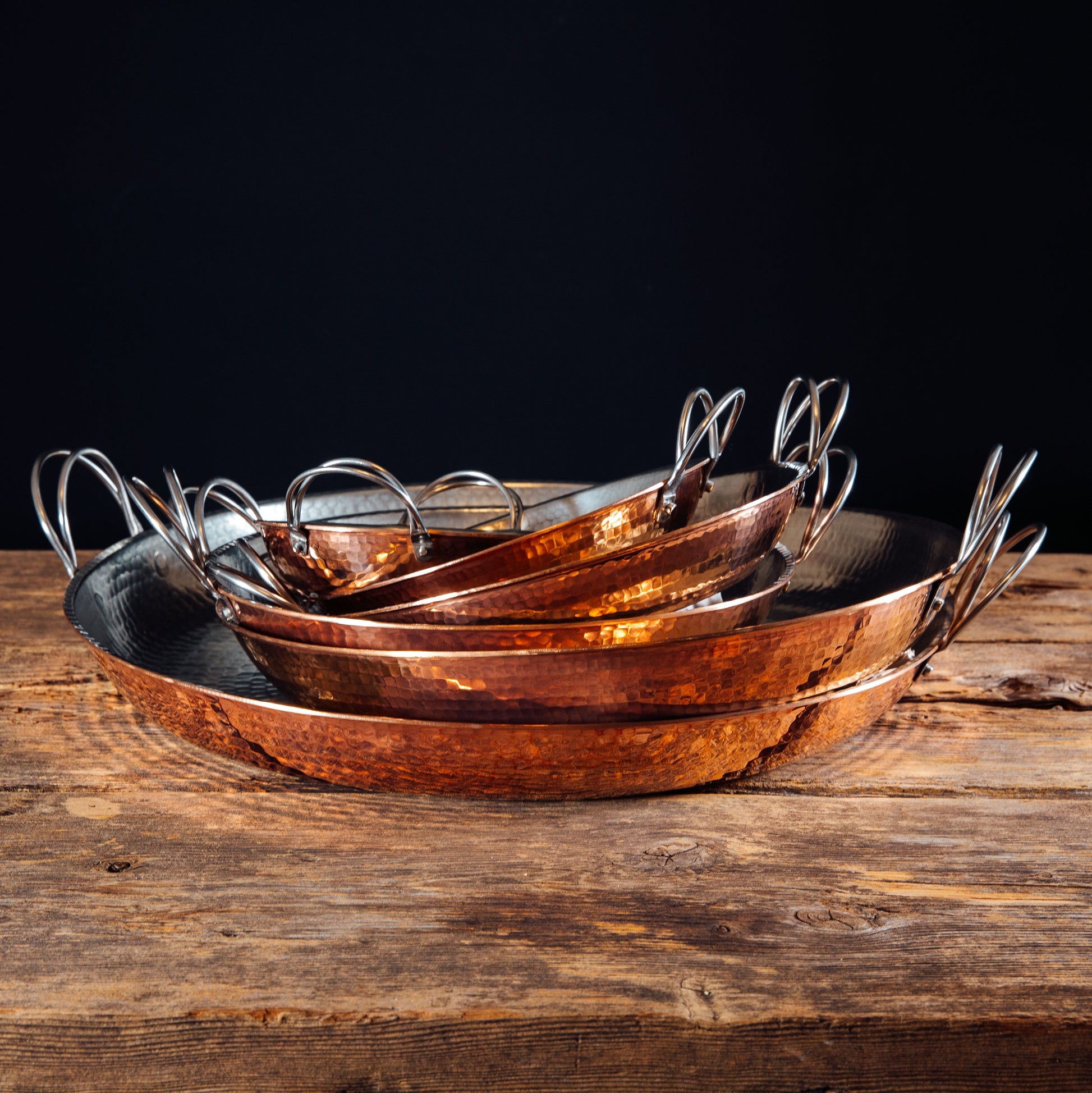 Set of six Alicante Copper Paella Pans by Sertodo, showcasing various sizes with handles and polished copper finish.