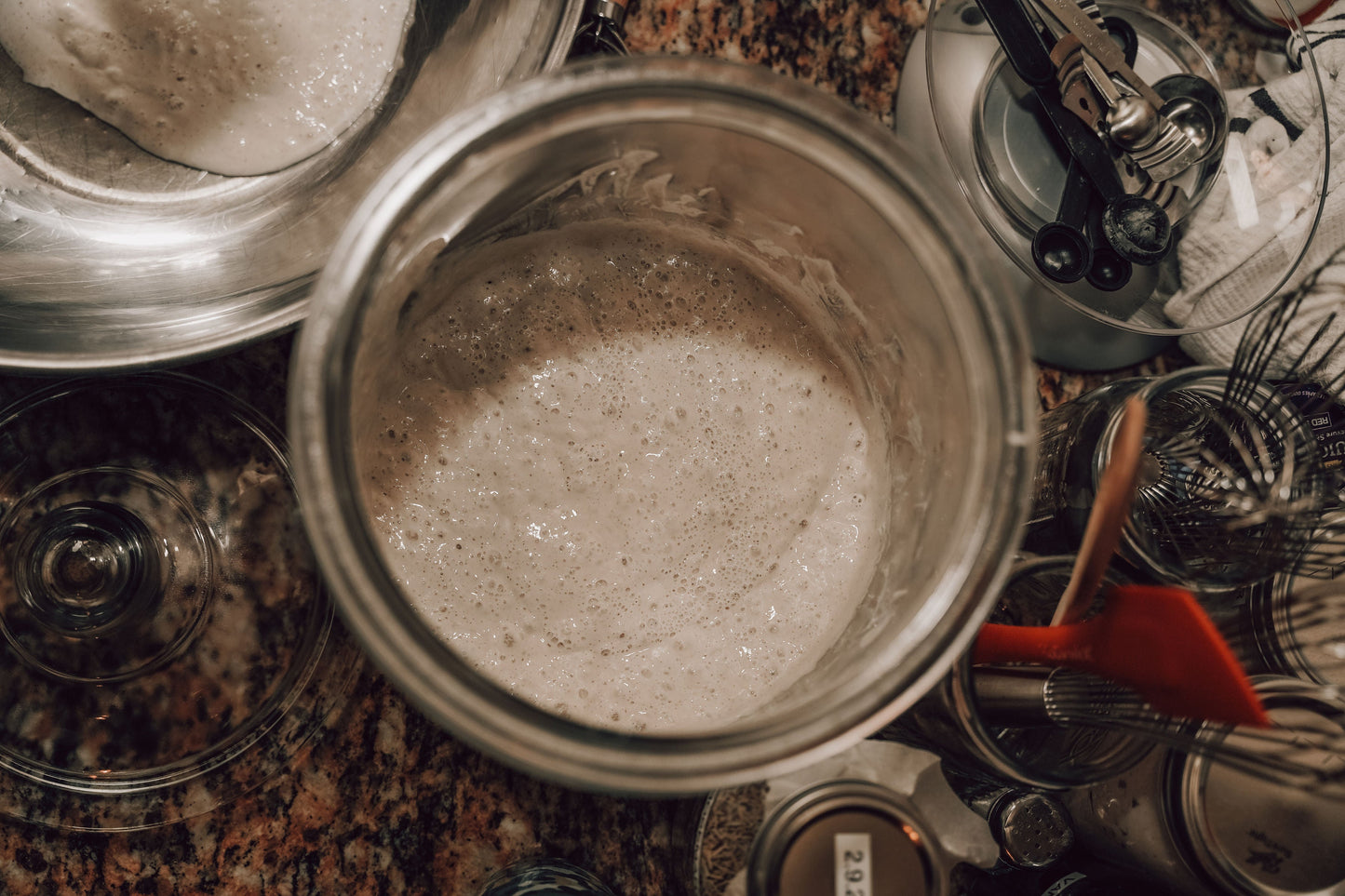 Onic Brands LLC sourdough starter in a glass jar, showing a bubbly, active fermentation with a lid and spoon inside.
