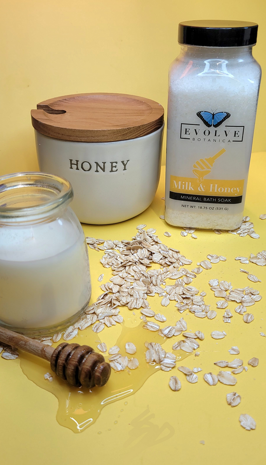 Evolve Botanica Mineral Soak Milk & Honey bath salt in a jar, with a scoop and honeycomb, showcasing relaxing bath essentials.