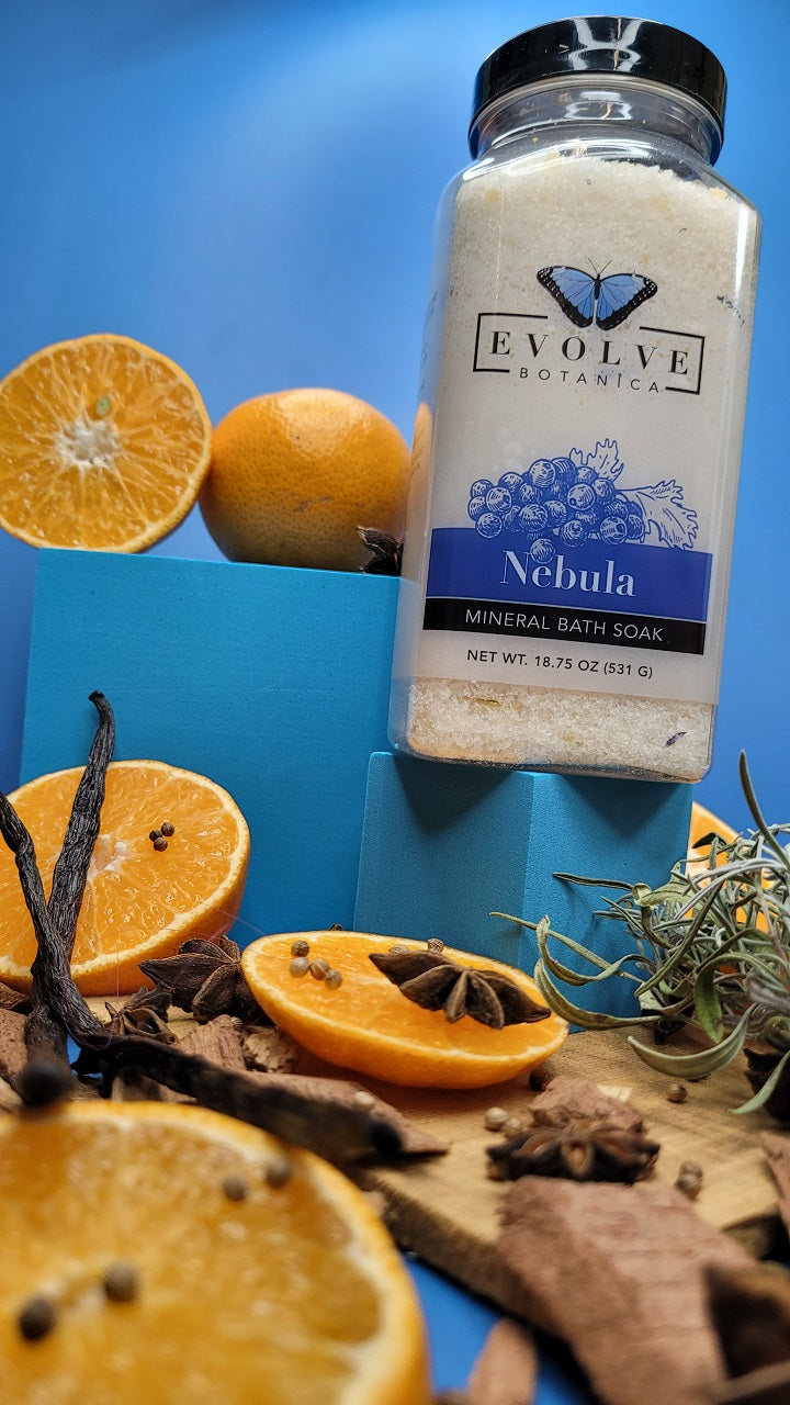 Evolve Botanica Mineral Soak Nebula bath salt in a glass jar with label, surrounded by natural spa elements and soft lighting.