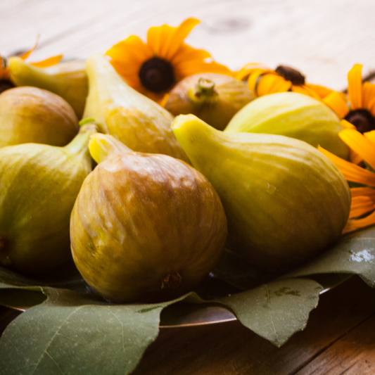 Fresh Marseilles Fig from The Farm On Central, showcasing ripe, juicy figs with green leaves on a rustic background.
