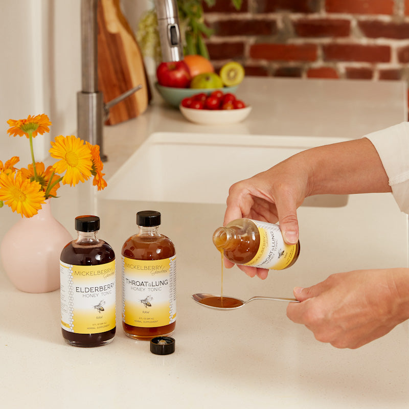 Pour of Mickelberry Gardens Elderberry Honey Tonic in a glass bottle, showcasing its rich, golden color and smooth texture.