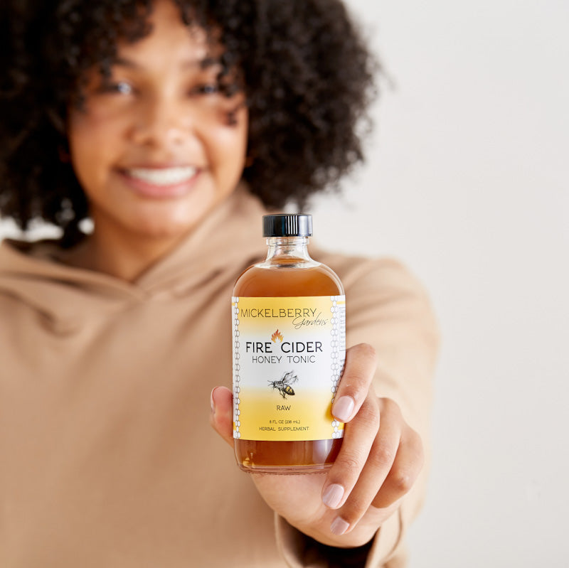 Mickelberry Gardens Fire Cider Honey Tonic in an 8oz bottle held by a person, featuring a honey tonic with fiery spices and honey.