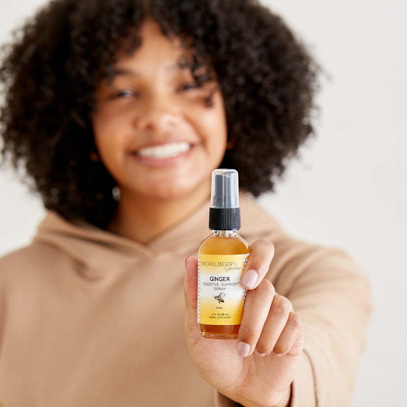 Mickelberry Gardens ginger digestive support spray in a 2oz bottle, held by a model, featuring honey tonic for digestion aid.