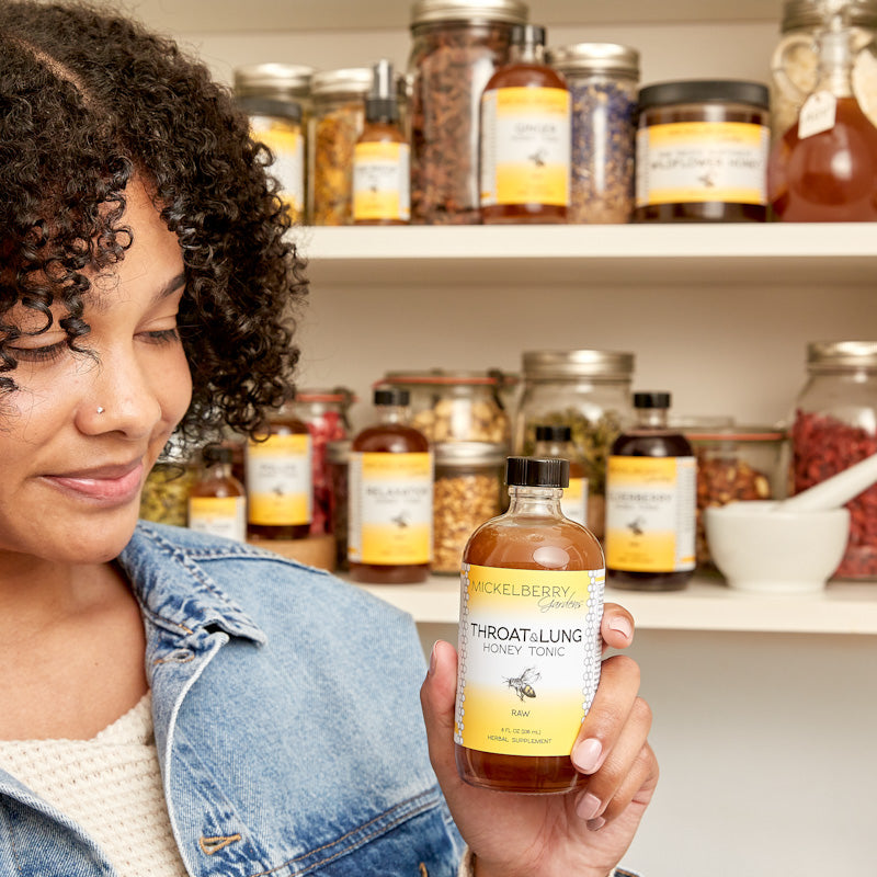 Mickelberry Gardens throat and lung honey tonic in a glass bottle, held by a person, with honey and herbal ingredients visible.