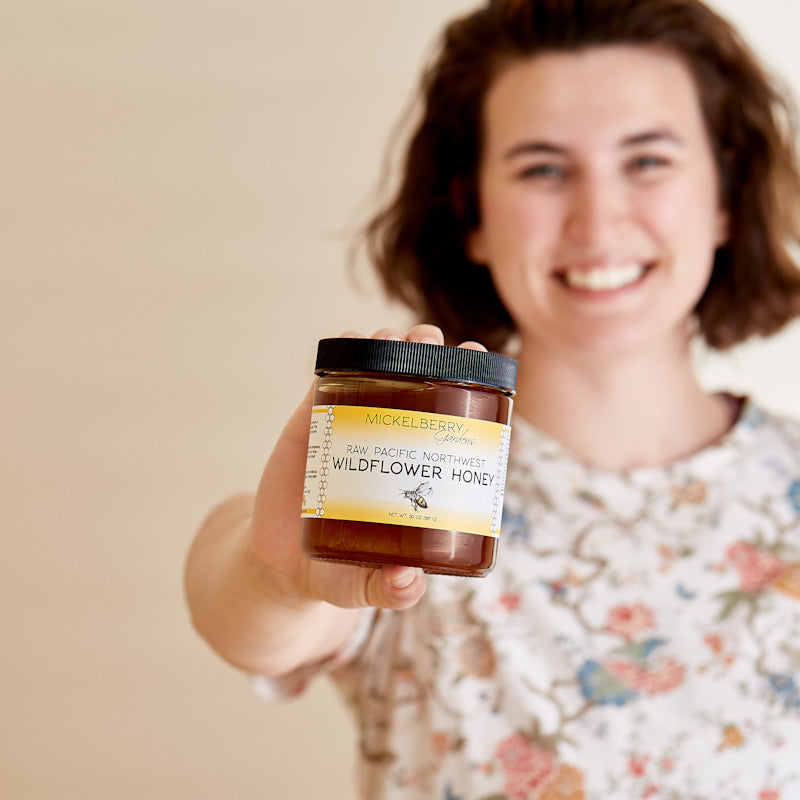 Jar of raw local honey showing honey varietals from Mickelberry Gardens, with golden honey and natural honeycomb pieces visible.