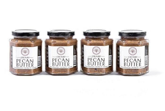 Four jars of Millican Pecan creamy pecan butter in a country store setting, showcasing the smooth, nutty spread in clear jars.