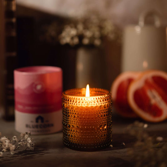 Bluecorn Candles Paloma scented candle in clear glassware with a soft, warm glow and floral label design.