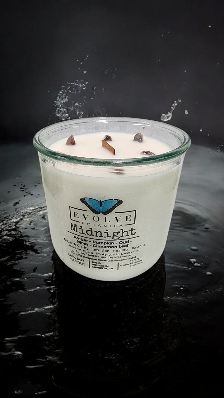 Evolve Botanica Midnight Rocks Candle with wood wick and super seven gemstone soy candle burning in a cozy setting