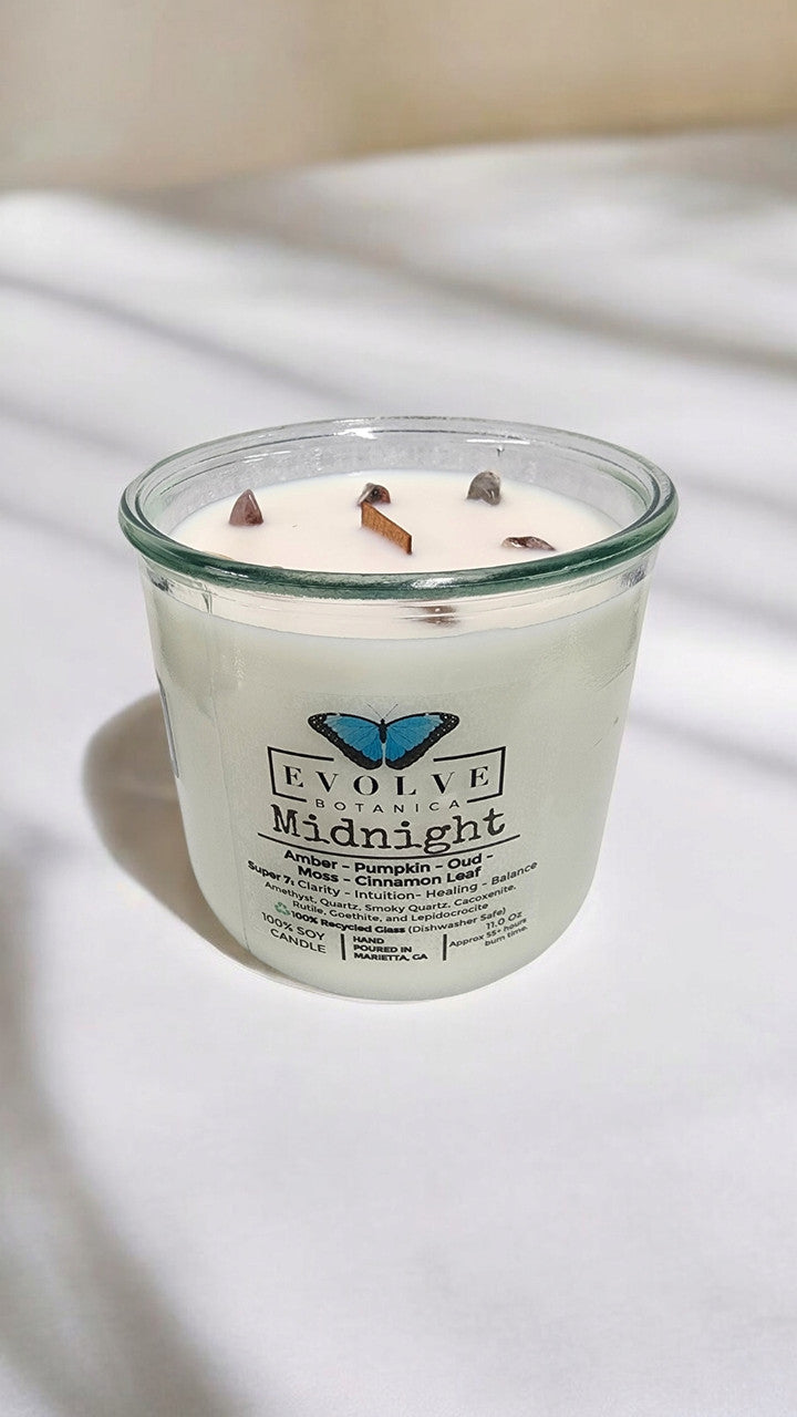 Evolve Botanica Midnight Rocks Candle with wood wick and seven gemstone soy candle, dark-colored glass jar, lit for ambiance
