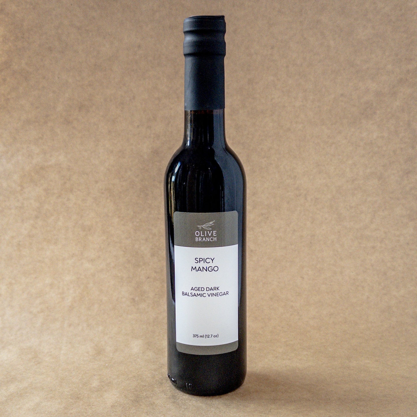 Spicy mango aged dark balsamic vinegar in a glass bottle, produced by Olive Branch Oil & Spice, showcasing rich colors and spiced mango flavor.