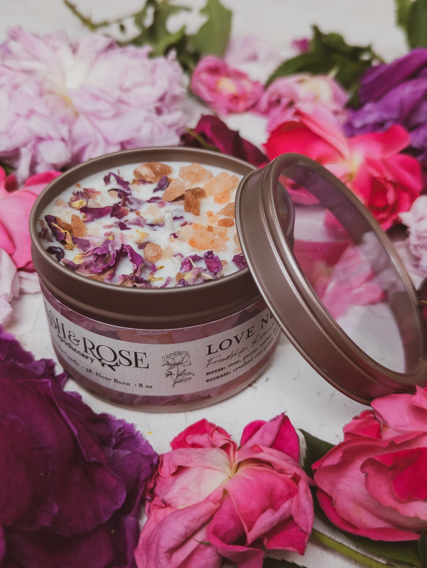 Ash & Rose Love Notes Rose and Pink Salt Candle, 4 oz, with a soft pink wax finish and a burning wick, creating a cozy ambiance.