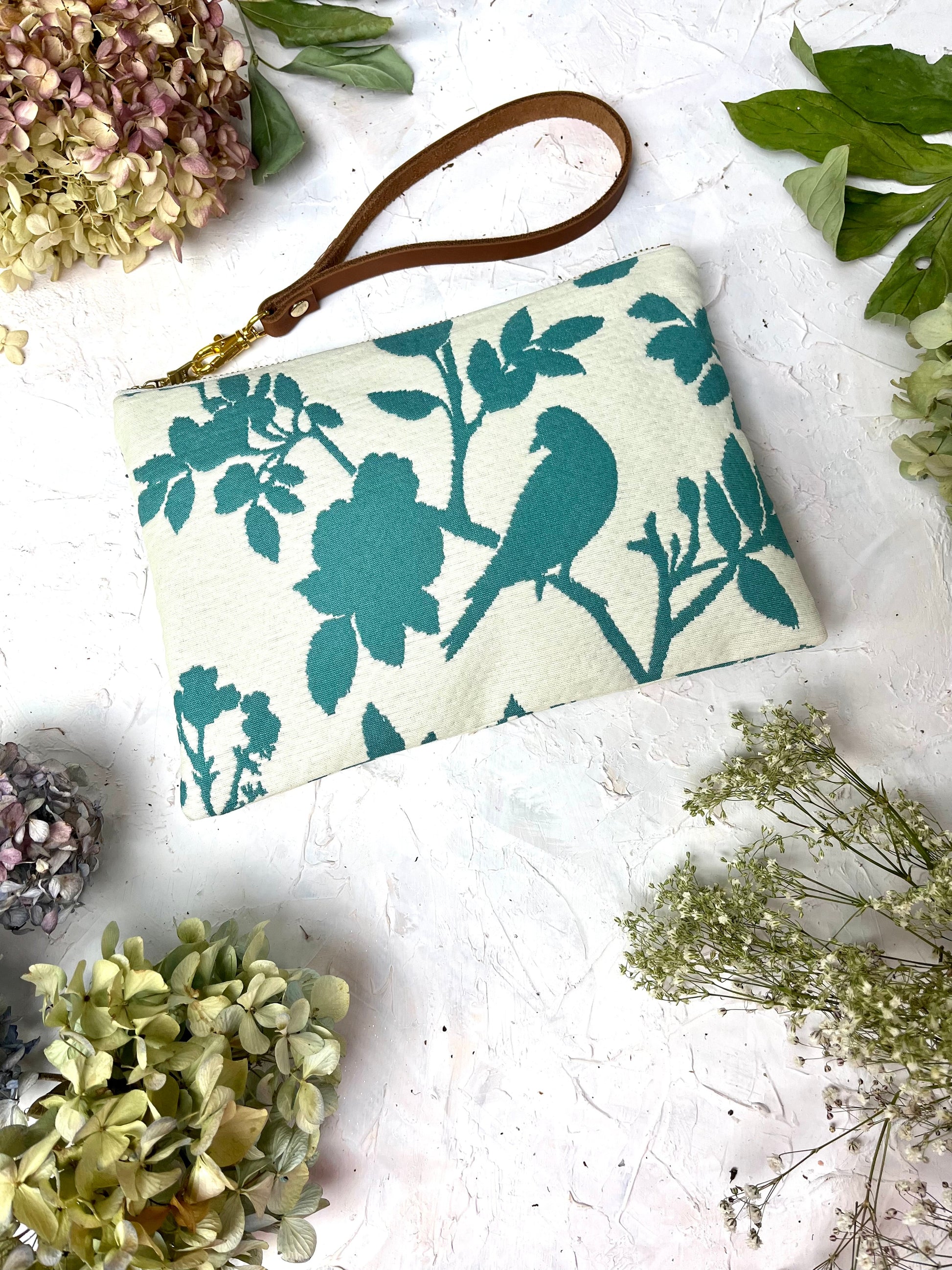 Ash & Rose bird silhouette wristlet purse with a sleek design, featuring a wrist strap and decorative bird pattern.