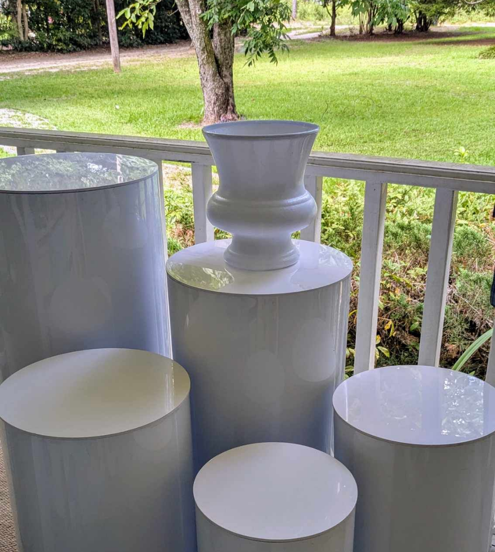 White pedestal stand and cylindrical tables for event rentals, perfect for gatherings, by Blessings Grow Meadows Merch in Metter, GA