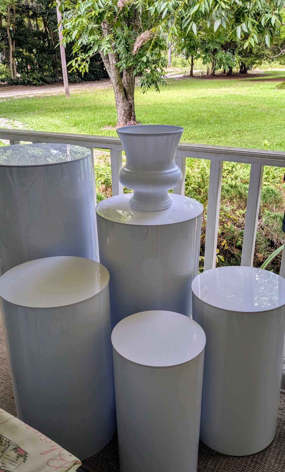 White pedestal stand and cylinder tables for event rentals by Blessings Grow Meadows Merch, ideal for elegant gatherings.
