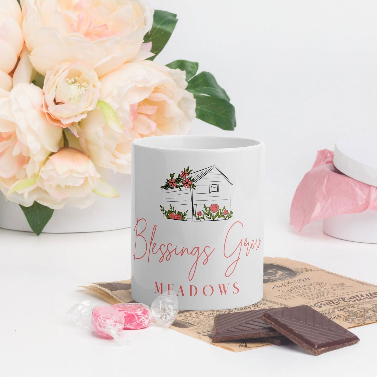 White glossy Blessings Grow Meadows mug featuring the Blessings Grow Merch logo and a smooth, reflective surface.