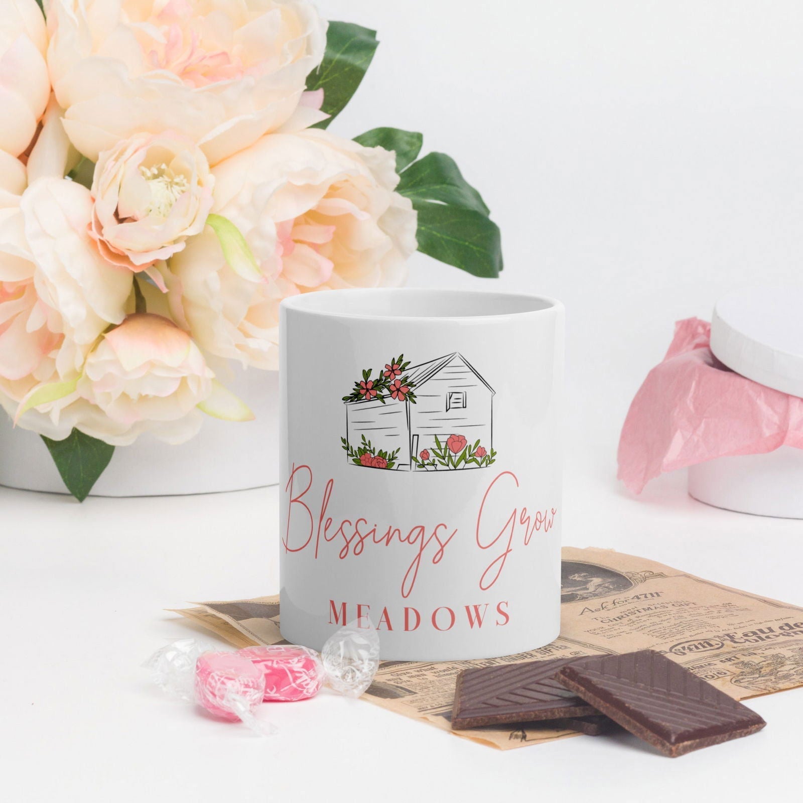 White glossy Blessings Grow Meadows mug featuring the Blessings Grow Merch logo and a smooth, reflective surface.