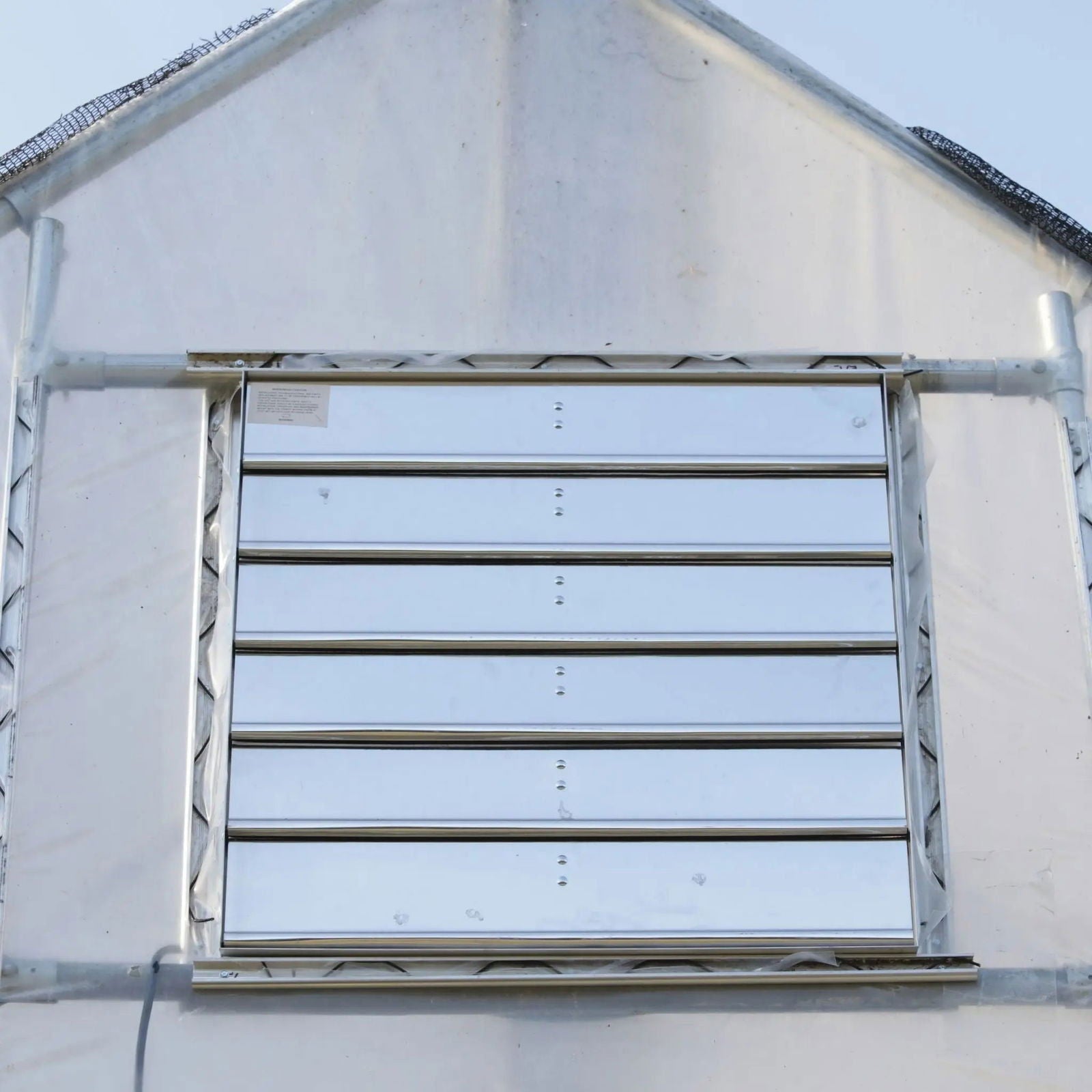 Greenhouse shutter mount exhaust fan by Bootstrap Farmer, green metal fan with protective grille for ventilation.