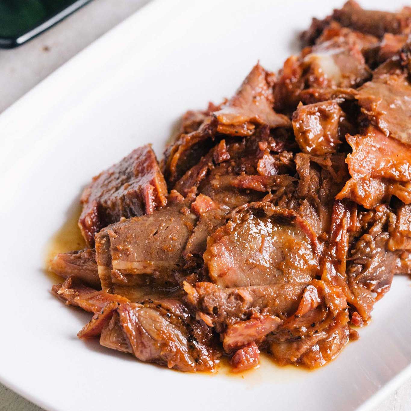 Slow smoked BBQ brisket from Pig of the Month BBQ, topped with sauce, showcasing tender, flavorful meat ready to serve.