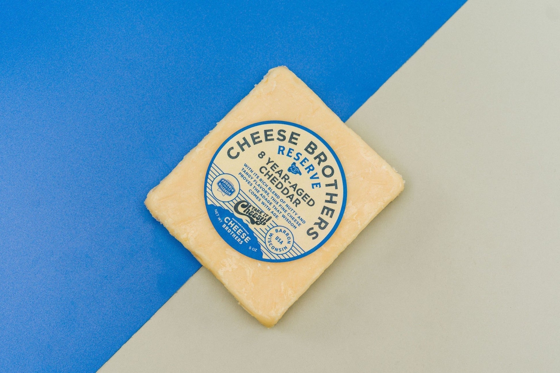 A block of 8-year-aged cheddar cheese from Cheese Brothers, Inc., showcasing its firm texture and deep orange color.
